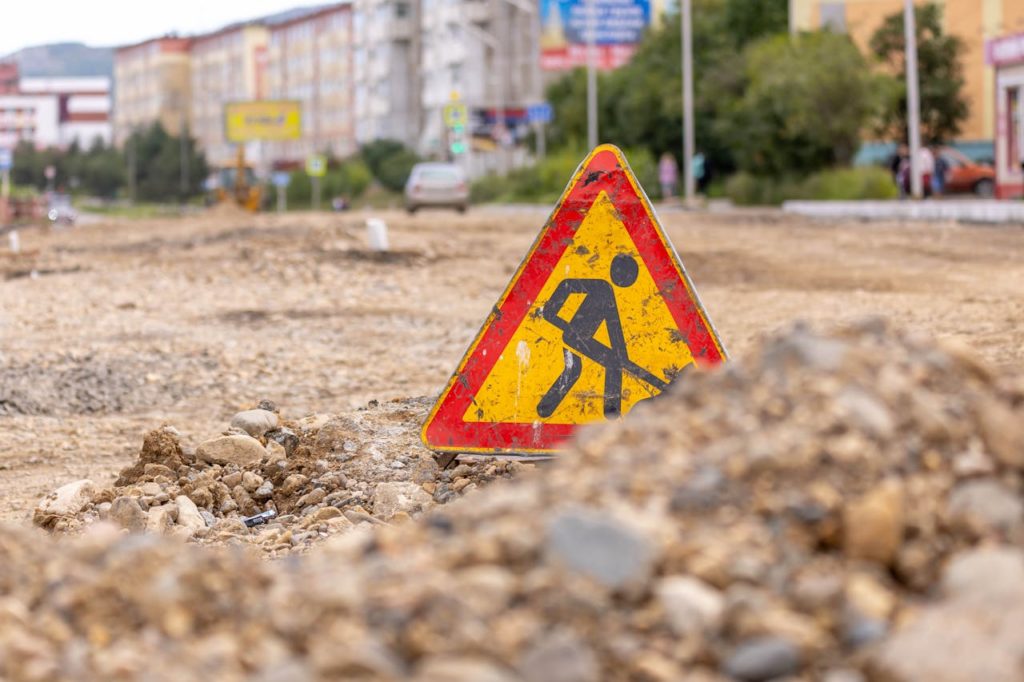 Yellow triangle warning sign indicating road work on an urban street under construction.